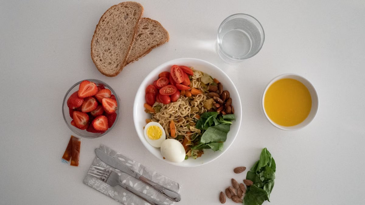 A balanced meal featuring a variety of healthy ingredients including noodles, eggs, almonds, strawberries, and fresh vegetables.