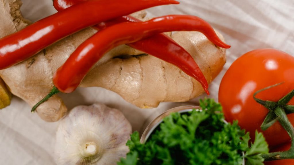 Close-up of fresh ingredients including chili peppers, ginger, and tomatoes on a white fabric surface.